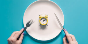 hands-holding-knife-fork-alarm-clock-plate-blue-background