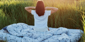 slim-female-with-dark-hair-wearing-white-casual-t-shirt-posing-backwards-with-raised-arms-stretching-hands-after-sleeping-enjoying-sunrise-green-meadow-beautiful-nature